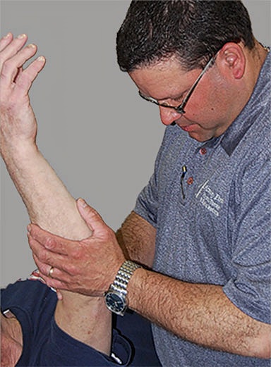 Kevin-Office Physiotherapist stabilizing a patient’s raised leg during a physical therapy range-of-motion exercise.